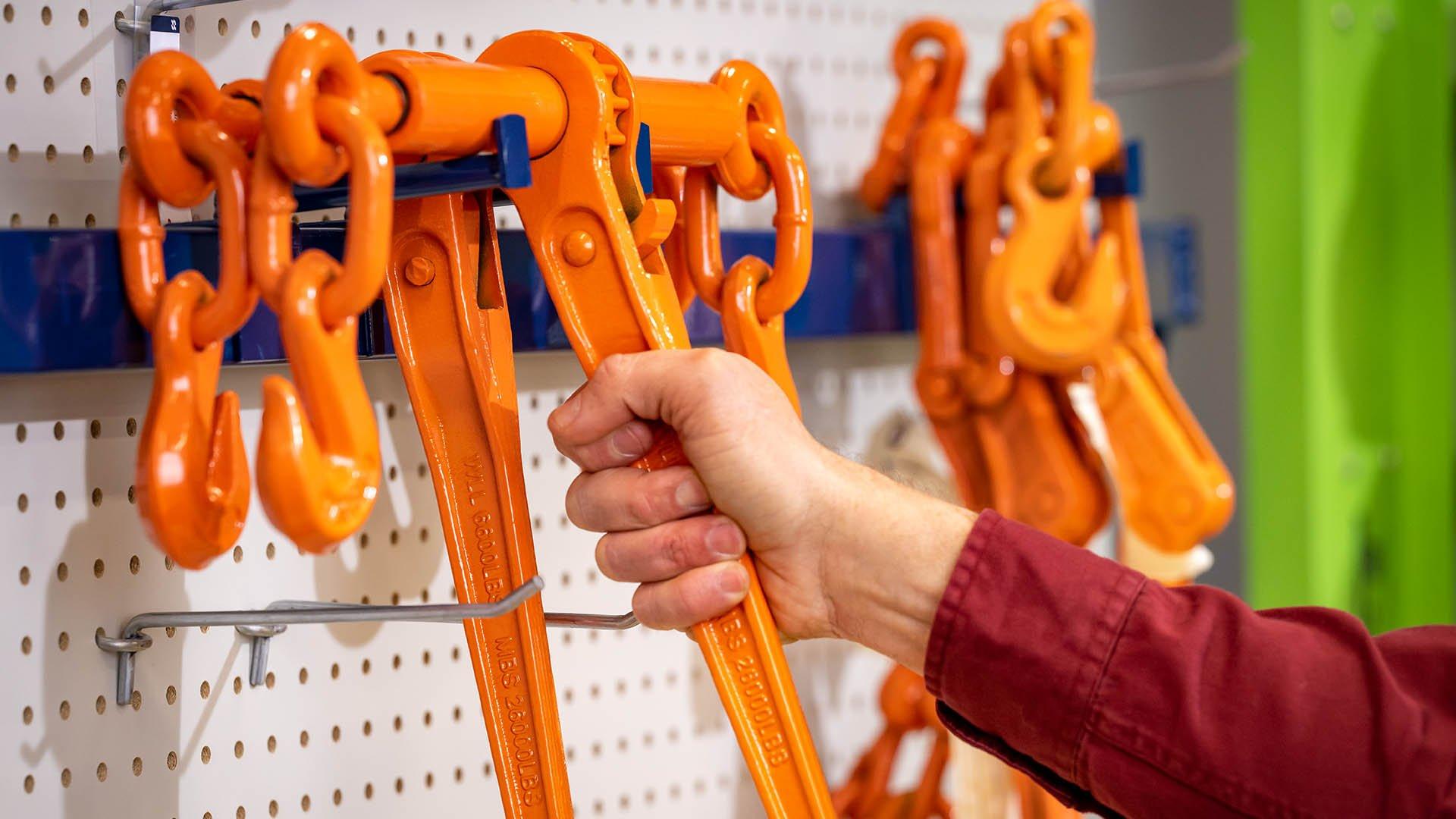 Close up of a hand grabbing an orange tool from sales rack at Ferguson counter.