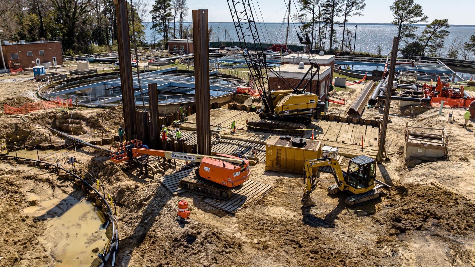 Construction site of a water treatment plant, with excavators, cranes and front-end loaders, next to a lake.