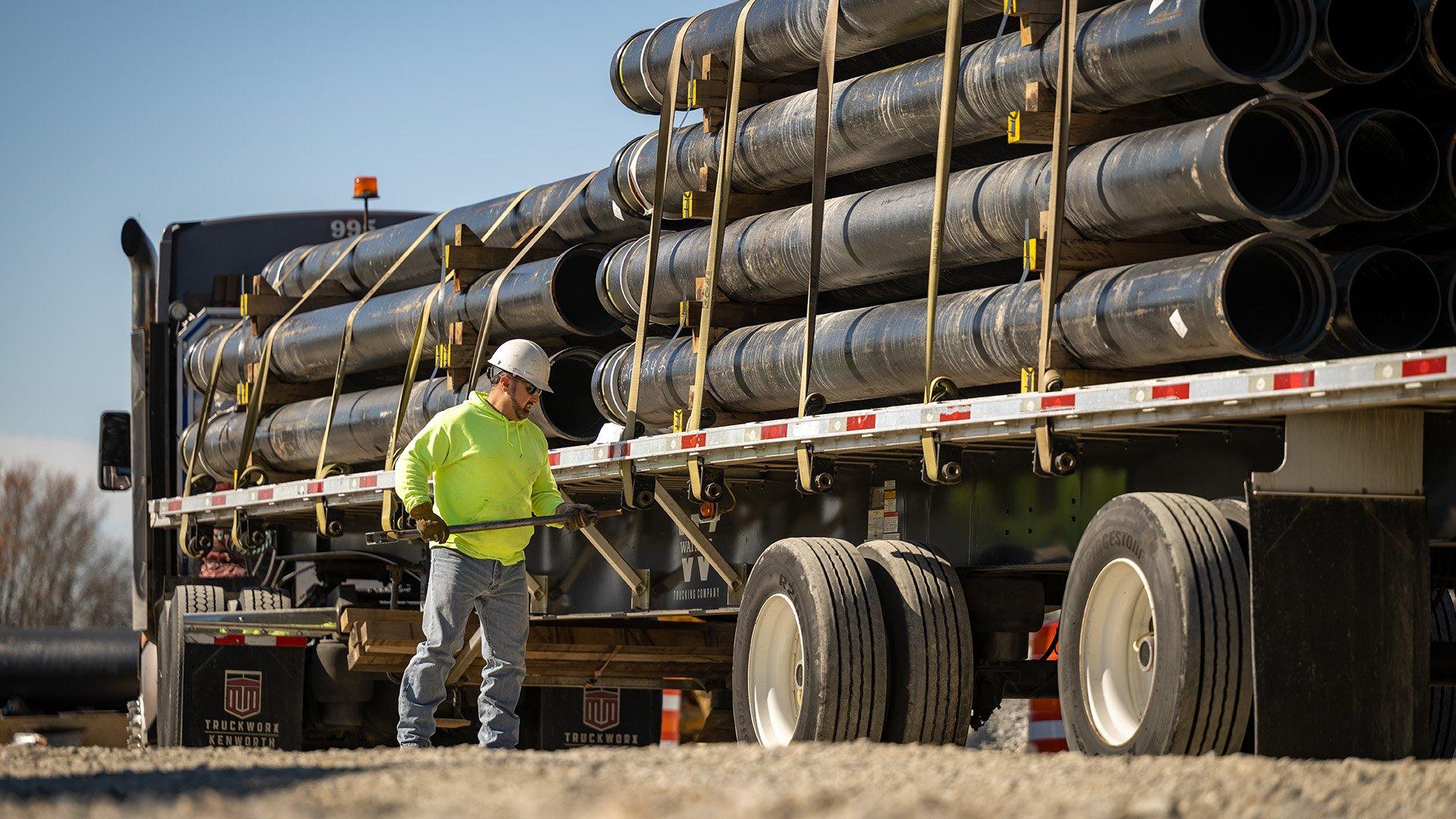 A flat-bed truck carrying pipe arrive at jobsite.
