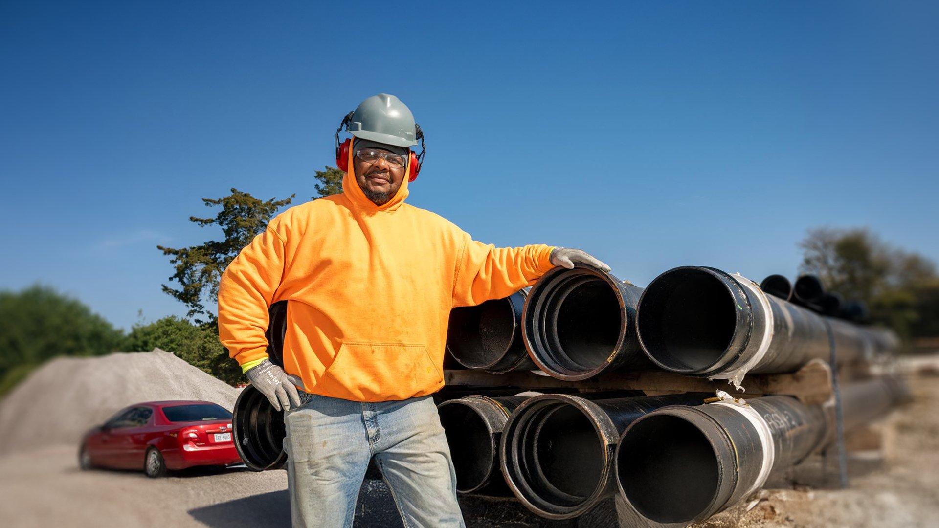 A contractor wearing PPE standing next to a stack of pipe on a flatbed.