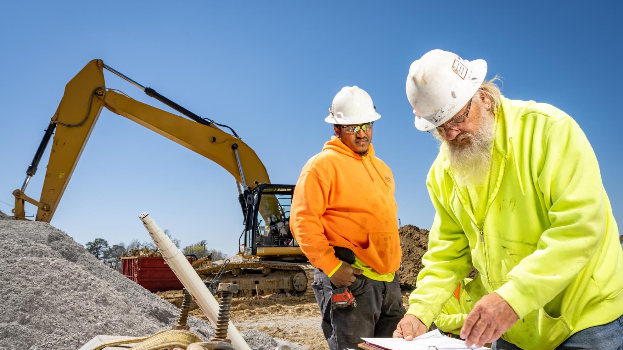 Two workers wearing hard hats on a construction jobsite review plans.