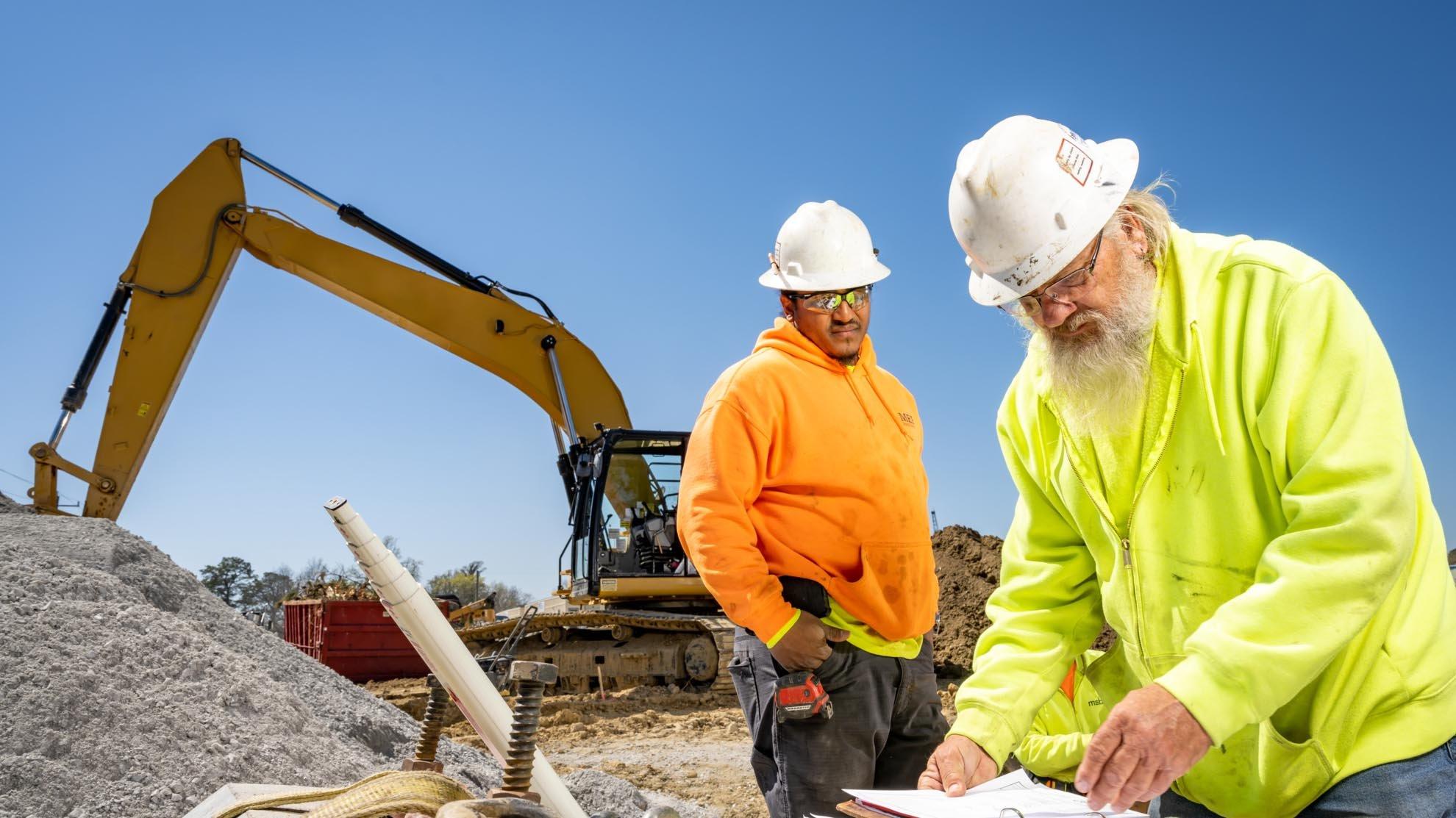 Two contractors on a jobsite review plans in a binder.