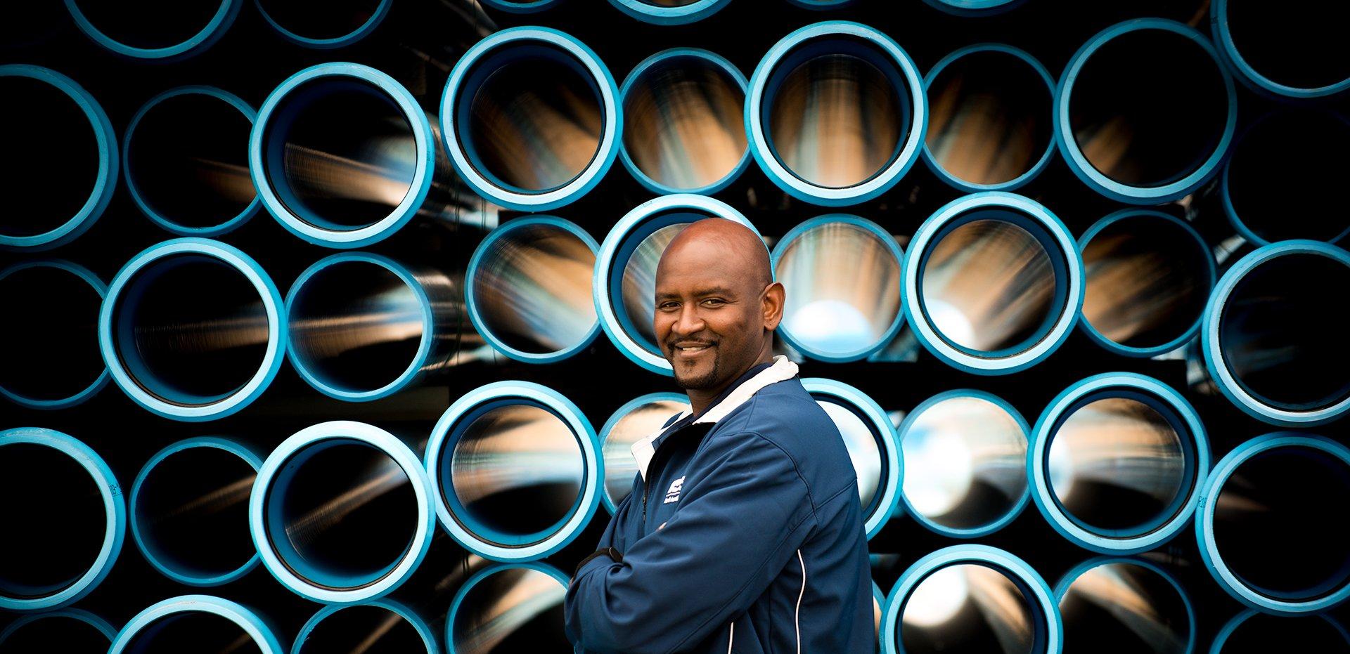 A Ferguson associate smiles in front of a stack of pipe with open ends facing the viewer.
