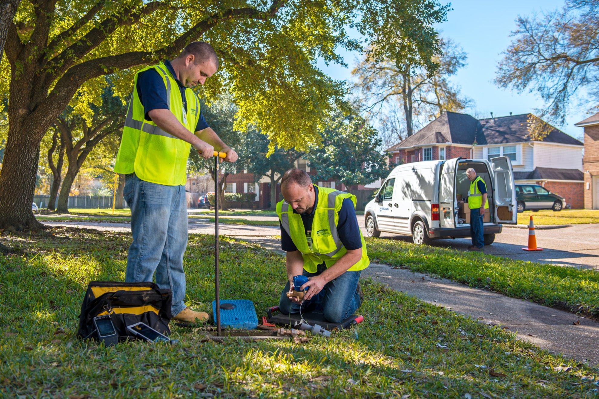 Three workers outside a parked Ferguson Waterworks van install a water meter in a front yard.