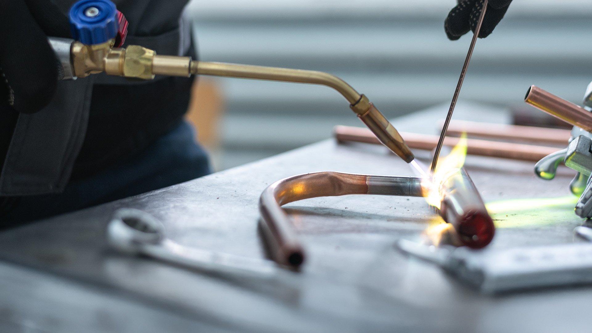 Close up image of brazing rod and torch used on copper pipe to braze two metals together. 