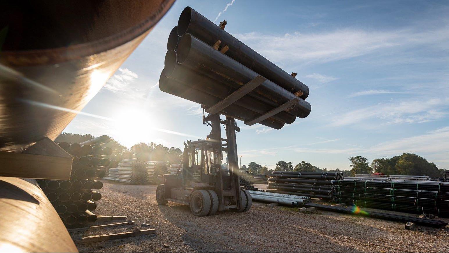 A construction forklift hauls a stack of large industrial pipe at a jobsite.