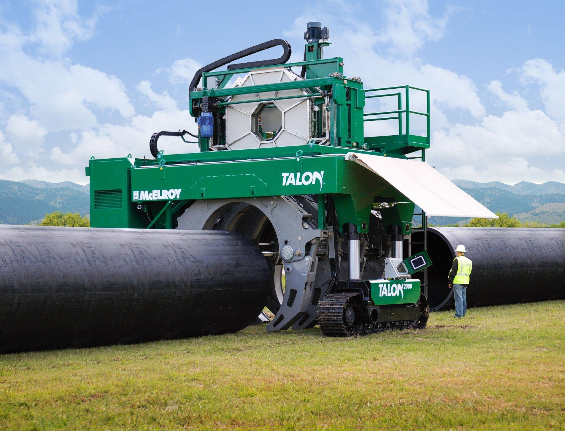 A large McElroy Talon fusion machine posed over two large pipes in a field.