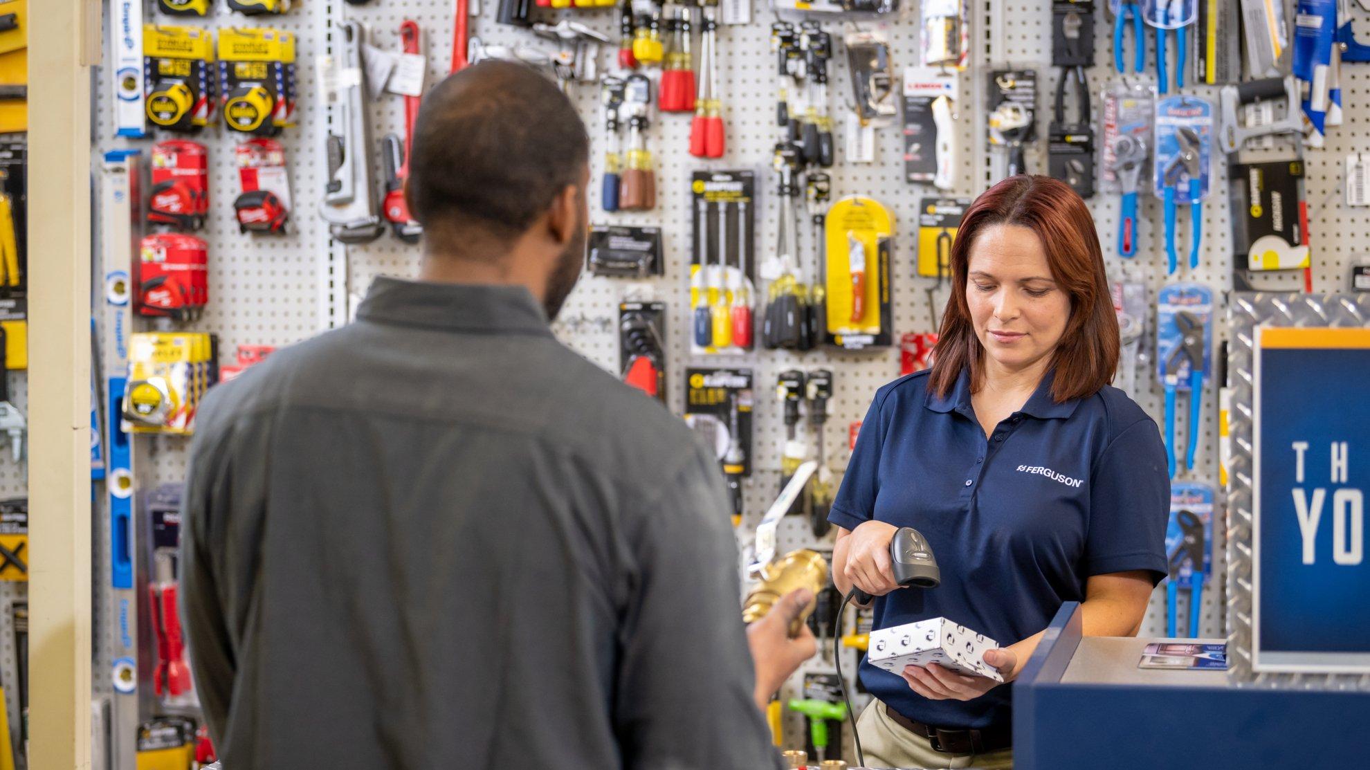 A Ferguson associate behind a counter scans a product for a customer.