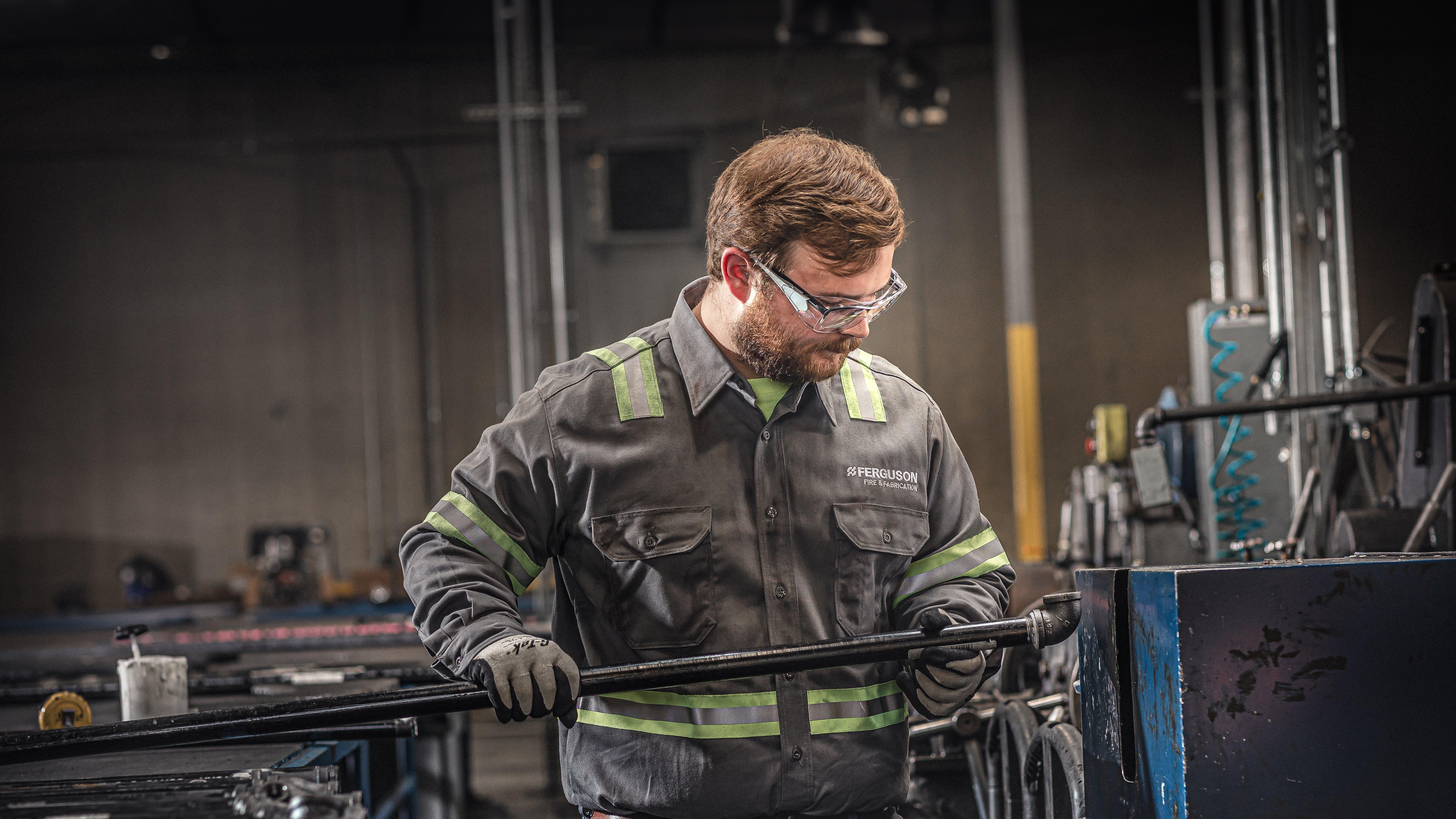 A Ferguson Fire & Fabrication associate wearing safety glasses examines a pipe fitting.