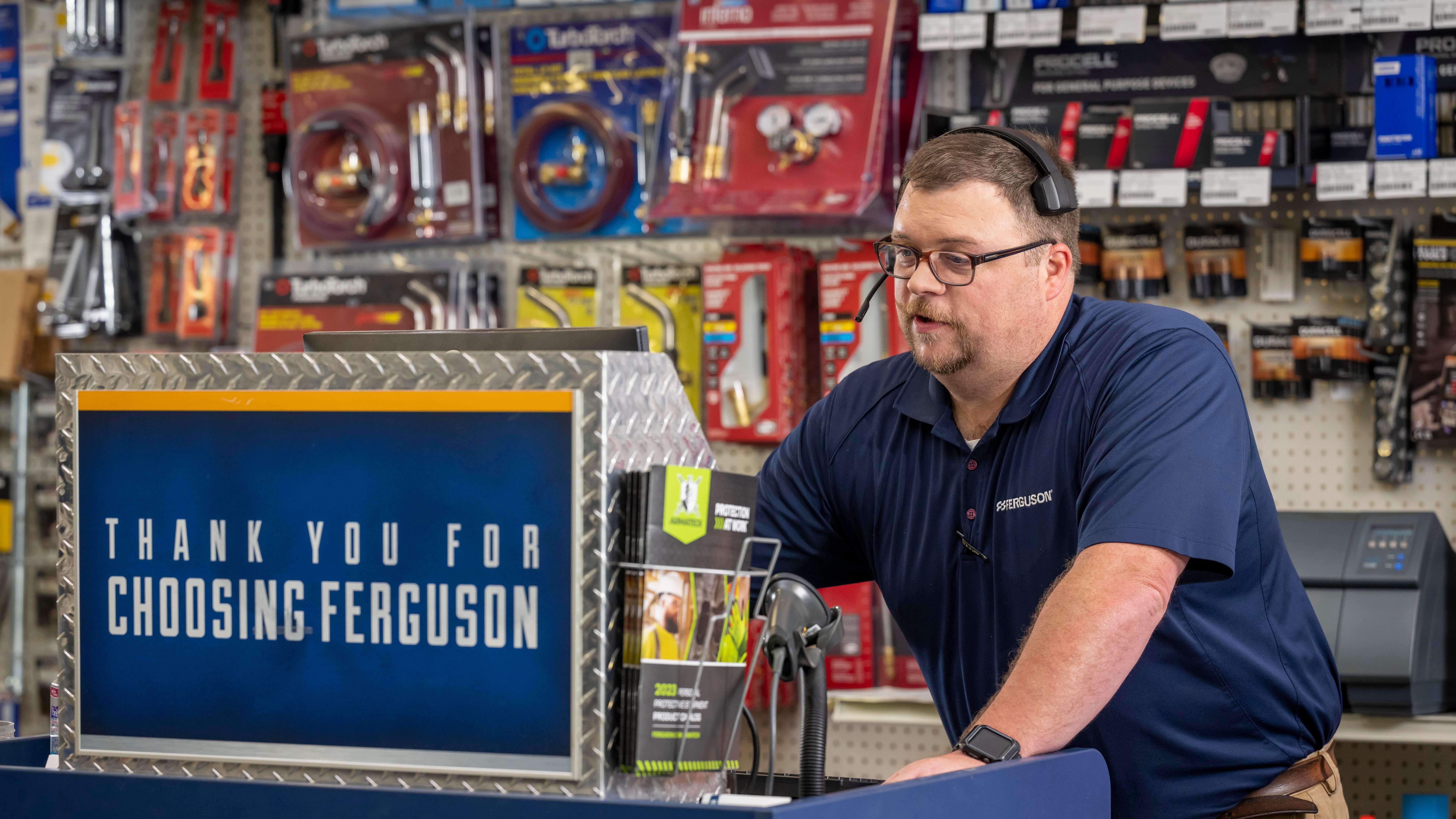 A Ferguson associate behind the counter speaks into a phone headset while looking at his computer.