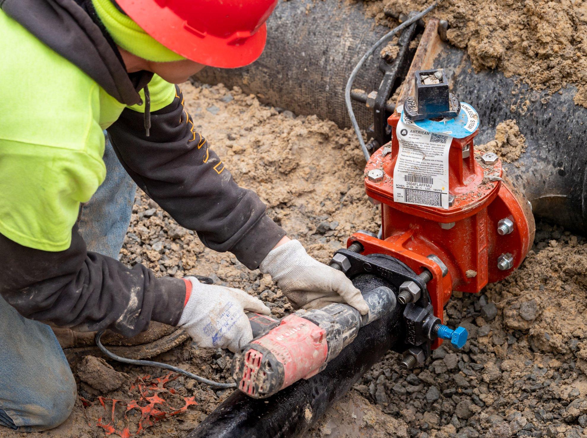 A worker connects a water line tap to an underground pipe.